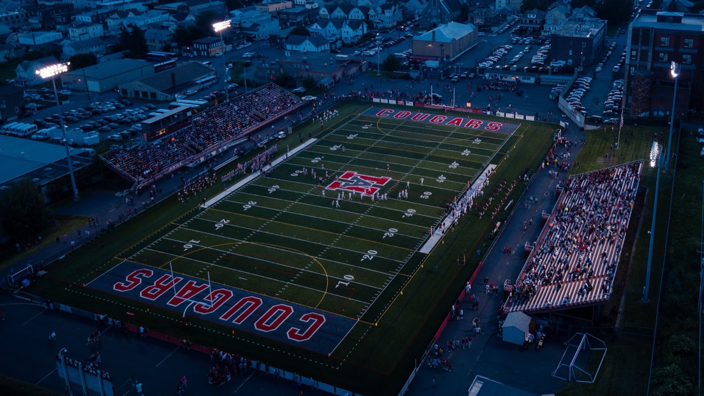 Aerial view of a football stadium glowing under Friday night lights