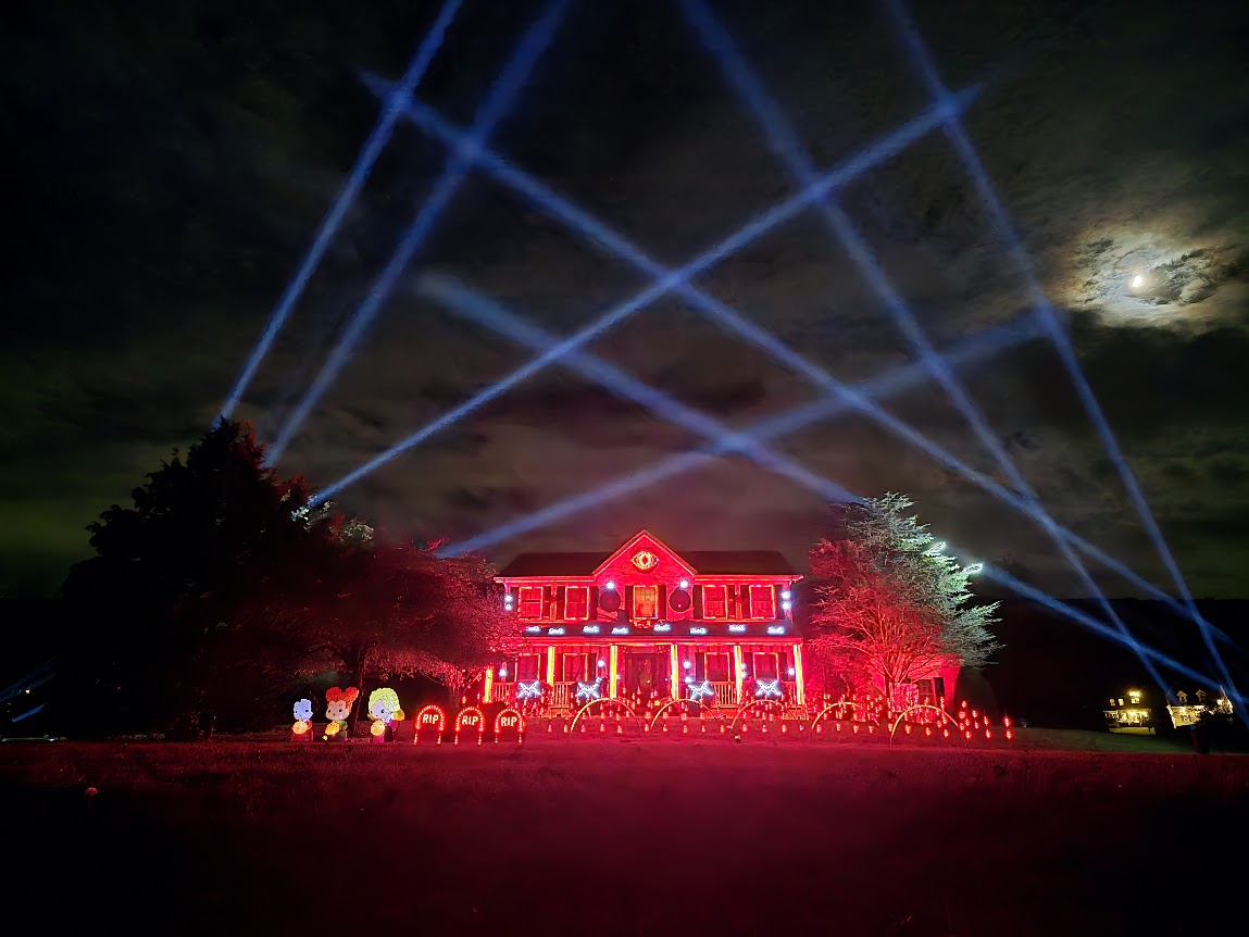 Halloween light show with a red-lit house and skybeams crossing the night sky